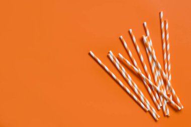 Çizgili kağıt, turuncu arka planda pipet içiyor. Çevre dostu ve geri dönüşümlü.