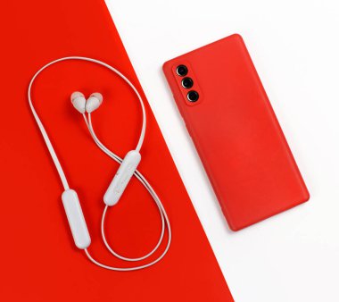 Kırmızı ve beyaz kablosuz kulaklıklı akıllı telefon kırmızı ve beyaz arka planda üst görünüm