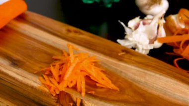 Kadının elleri, tahta bir tahtaya rendeleyici ve taze havuç koyuyor.