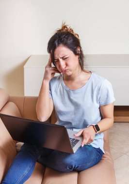 Evde kanepede otururken dizüstü bilgisayarla çalışan stresli genç kadınlar.