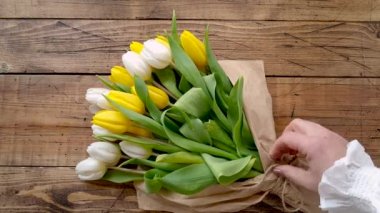 Eller ahşap masa manzaralı bir lale buketini çözer. 