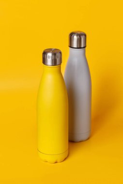 Sarı ve gri, sarı arka planda yeniden kullanılabilir çelik şişeler. Sıfır atık ve sürdürülebilir yaşam tarzı kavramı