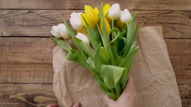 Tahta bir masanın üstünde sarı ve beyaz lalelerden buket yapıyorum. 