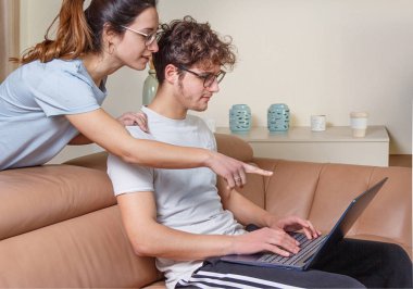 Genç kadınlar ve erkekler evdeki bej kanepede otururken dizüstü bilgisayarla çalışıyorlar. Kadınlar dizüstü bilgisayarı elle işaret eder.. 