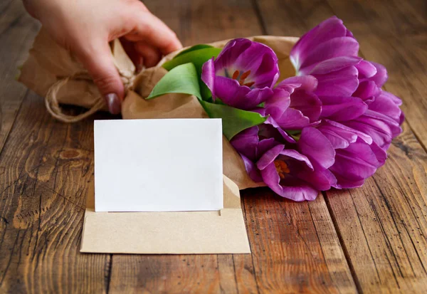 Hand Mit Lila Tulpen Blumenstrauß Und Leere Karte Auf Holztisch — Stockfoto