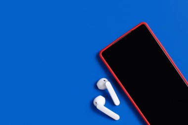 Akıllı telefon ve beyaz kablosuz kulaklıklar. Mavi arka planda üst görünümü olan.