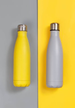 Grey and yellow insulated reusable bottles on grey and yellow background top view