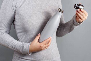 Close up of woman in grey tee opening grey insulated bottle on yellow background