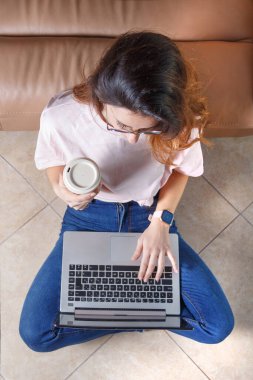Young women using laptop and drinking coffe to go while sitting on the floor at home top view