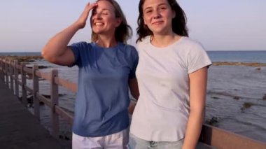 Anne ve kızı gün batımında deniz kenarında duruyor.