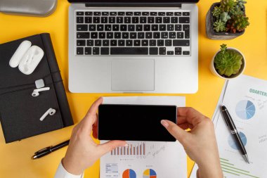 İş kadını elleri dizüstü bilgisayarın yanında cep telefonu tutuyor ve rapor veriyor. Modern ofis sarı masa üstü görünümü