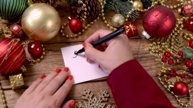 Kadının eli ahşap masaya Noel süsleri asılmış bir karta satış yazısı yazıyor.