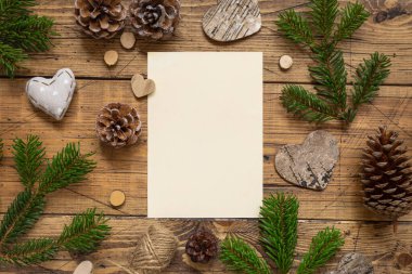 Tahta bir masanın üstünde boş bir kartla Kış Noel Kompozisyonu. Noel ve Yeni Yıl tebrik kartı şablonu köknar ağacı dalları, çam kozalakları ve Noel süslemeleri. Tatil modeli.