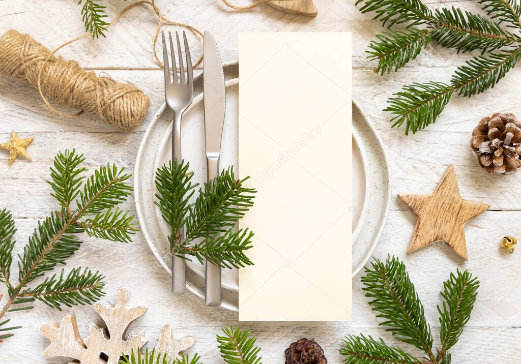 Festive table setting of plates, cutlery and fir tree branches top view. Mockup of Christmas or New Year menu on white wooden table, copy space. Winter wedding, restaurant holiday catering