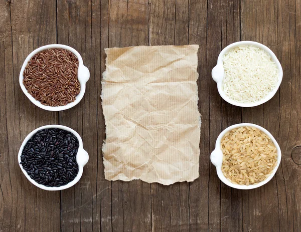 Variedad de arroz en cuencos sobre mesa de madera y papel viejo —  Fotos de Stock