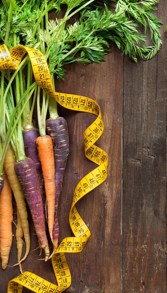 Fresh organic rainbow carrots and yellow measuring type — Stock Photo, Image