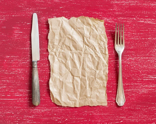 Vintage fork and knife with craft paper on red wood — Stock Photo, Image