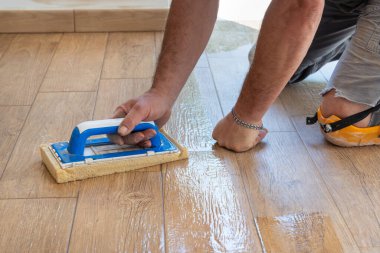 Zemini süngerle temizleyen bir zanaatkar dizlerinin üstünde oturuyor, eli yakın. Döşeme konsepti. Bir binanın inşaatı veya tadilatı sırasında çalışan erkekler