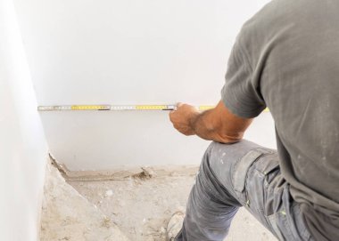 Zanaatkar duvar arkasını ölçüyor, sarı katlanabilir bir cetvel tutuyor, yakın plan. Ev iç dekorasyonu. Yeni bir binanın inşaatı. DIY Ev geliştirme