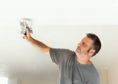 Tozlu zanaatkar, odanın içinde tavana sıva yapıştırmak için mala ve şahin kullanır. İnşaat sırasında ya da bir evin tadilatı sırasında gri tişörtlü adamlar. DIY Ev geliştirme