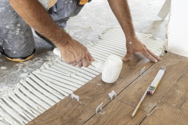 İşçi seramik fayansları yapıştırıcı yüzeyine yerleştiriyor, kauçuk çekiçle düzleştiriyor, kirli elleri yakınlaştırıyor. Bir evin inşaatında ya da yenilenmesinde çalışan zanaatkar, DIY ev imalatçıları