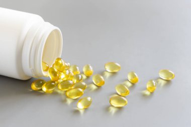 Sarı yumuşak jeller (jelatin kapsüller) ve gri yakın plan bir şişe, kopyalama alanı. Gıda desteği - Omega 3 Balık yağı veya sarımsak yağı, A vitamini, D3 veya E.
