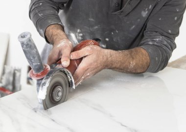 Gri gömlekli zanaatkar, gri mermer bir fayans kesiyor. İşinin ehli bir adam, elleri yakın. Ev inşaatı ya da DIY yenilemesi. Uzman fayans kesme teknikleri