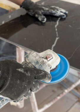 Gri tişörtlü zanaatkar, siyah seramik kenarı öğütücü kullanarak öğütüyor. İşinin ehli bir adam, elleri yakın. Ev inşaatı veya DIY yenilemesi