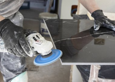 Gri tişörtlü zanaatkar, siyah seramik kenarı öğütücü kullanarak öğütüyor. İşinin ehli bir adam, elleri yakın. Ev inşaatı veya DIY yenilemesi