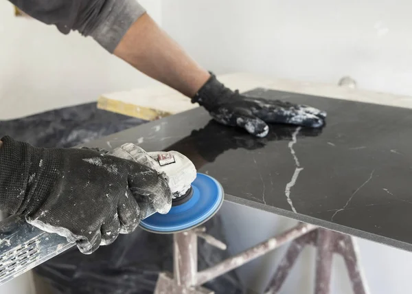 Gri tişörtlü zanaatkar, siyah seramik kenarı öğütücü kullanarak öğütüyor. İşinin ehli bir adam, elleri yakın. Ev inşaatı veya DIY yenilemesi