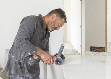 Gri gömlekli zanaatkar, gri mermer bir fayans kesiyor. Adam iş başında, elleri yakın. Ev inşaatı ya da DIY yenilemesi. Uzman fayans kesme teknikleri