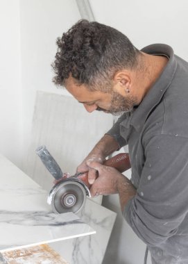 Gri gömlekli zanaatkar, gri mermer bir fayans kesiyor. Adam iş başında, elleri yakın. Ev inşaatı ya da DIY yenilemesi. Uzman fayans kesme teknikleri