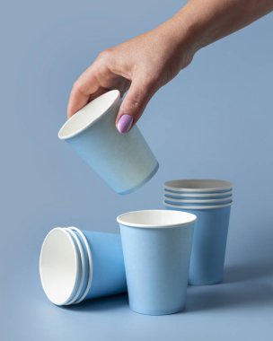 Tek kullanımlık açık mavi kağıt bardağı olan kadın el yakından izole edilmiş, reklam alanı olan bir model. Boş karton kahve fincanı. Kapaksız çevre dostu tek kullanımlık konteynırlar