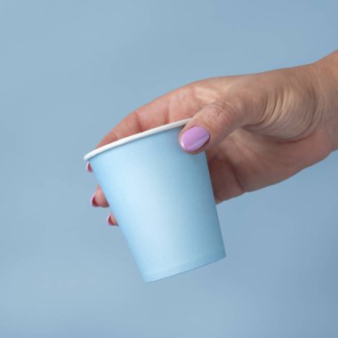 Tek kullanımlık açık mavi kağıt bardağı olan kadın el yakından izole edilmiş, reklam alanı olan bir model. Boş karton kahve fincanı. Kapaksız çevre dostu tek kullanımlık konteynırlar