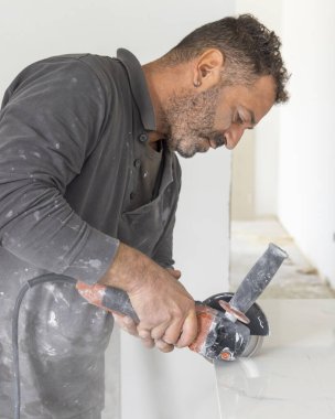Gri gömlekli zanaatkar, gri mermer bir fayans kesiyor. Adam iş başında, elleri yakın. Ev inşaatı ya da DIY yenilemesi. Uzman fayans kesme teknikleri