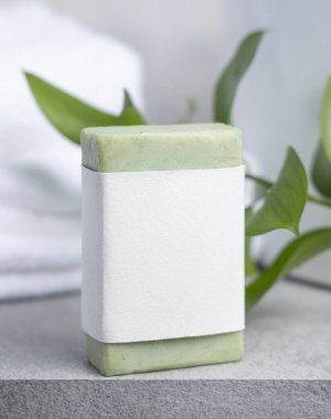 Yeşil etiketli yeşil sabun çubuğu ile yeşil yapraklı beyaz banyo havluları ile gri taş tezgahın üzerinde yakın çekim, ambalaj modeli. Doğal el yapımı bitkisel hijyen ürünü. Tarafsız tuvalet