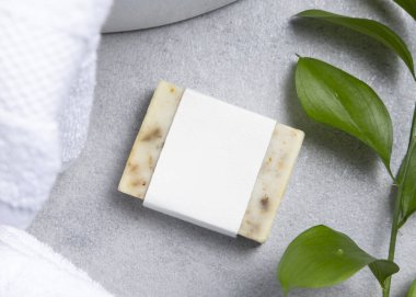 Yeşil yapraklı, beyaz banyo havluları ve gri taş tezgahın üzerinde boş etiketli krem sabun kalıbı kapatılıyor, ambalaj modeli yapılıyor. Doğal el yapımı bitkisel hijyen ürünü. Tarafsız tuvalet