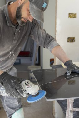 Gri tişörtlü zanaatkar, siyah seramik kenarı öğütücü kullanarak öğütüyor. İşinin ehli bir adam, elleri yakın. Ev inşaatı veya DIY yenilemesi