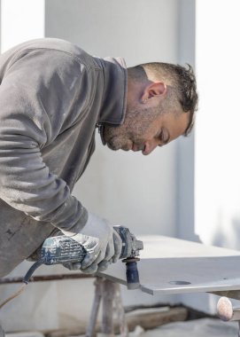 Kirli gri elbiseli bir zanaatkar seramik bir fayansta elmas kaplama ile delik açıyor. Adam iş başında, elleri yakın. Ev inşaatı veya DIY yenilemesi