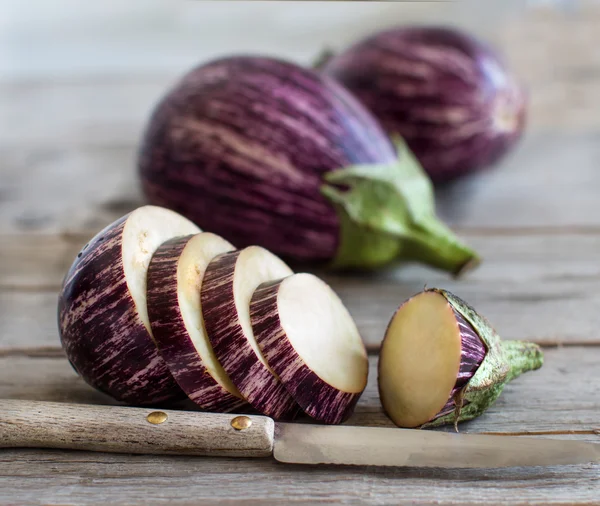 Färska råvaror randig äggplantor och skivor med kniv — Stockfoto