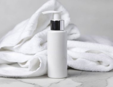 Beyaz boş pompa spa kozmetik şişesi. Otel banyosunda beyaz banyo terry havlusunun yanında. Gümüş metal yakalı plastik konteynır. Tarafsız arkaplan, alanı kopyala