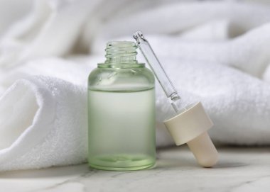 Pipette, beyaz bir havlunun yanında yeşil cam damlatan şişenin yanında. Etiketsiz cam kap, sıvı kozmetik ürünler için ambalaj modeli. Kopyalama alanı olan tarafsız arkaplan