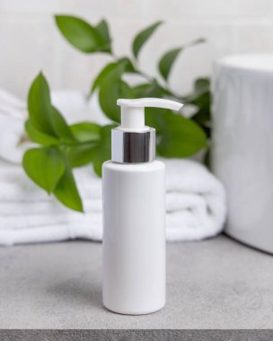 Paket maketi, beyaz boş bir pompa krem şişesi yeşil yapraklı dal, leğen ve beyaz banyo havlularına karşı banyodaki gri taş tezgahın üstünde. Doğal bitkisel kozmetik