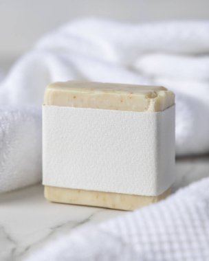 Beyaz banyo havlularının yanında boş kağıt etiketli bej, katı sabun kalıbının bir kopyası. Dikdörtgen şeklinde. Tarafsız arkaplanda fotokopi alanı olan markasız ambalaj. Kişisel bakım paketleme