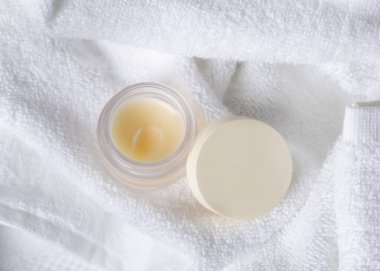 Beyaz havlu üzerinde boş kapaklı dudak kremi kavanozu, üst manzara. Tarafsız arkaplanda fotokopi alanı ile markasız kozmetik ambalaj. Spa otel banyosu içeriği