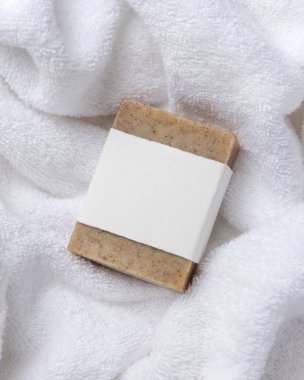 Beyaz banyo havlularının üzerinde boş kağıt etiket olan kahverengi sabun kalıbının bir kopyası. Dikdörtgen şeklinde. Tarafsız arkaplanda, fotokopi alanı ile markasız paketleme, üst görünüm. Kişisel bakım bağlamı