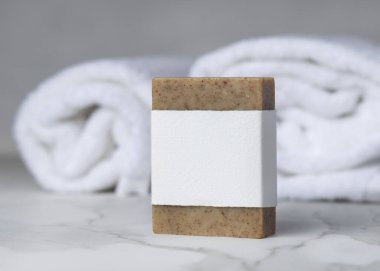 Beyaz banyo havlularının yanında boş kağıt etiketli kahverengi, katı sabun kalıbı. Tarafsız arkaplanda fotokopi alanı olan markasız ürün. Kişisel bakım bağlamı