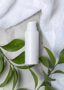 Beyaz Terry havlusunun yanında boş beyaz pompa şişesi ve taşın üstünde yeşil yapraklar, üst manzara. Kopya alanı ile markasız kozmetik paketleme. Cilt ürünüyle tarafsız banyo sahnesi