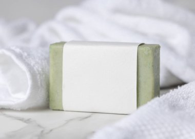 Beyaz banyo havlularının yanında boş kağıt etiketli bej, katı sabun kalıbının bir kopyası. Tarafsız arkaplanda fotokopi alanı olan markasız ürün. Kişisel bakım bağlamı