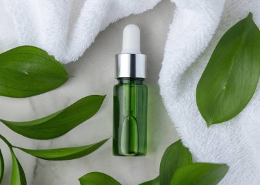 Beyaz havlu ve yaprakların yanında kapalı yeşil cam damlatıcı şişesi, taşın üstünde üst manzara, maket. Botanik tarzda spa ve otel cilt ürünleri için markasız kozmetik ambalajlama